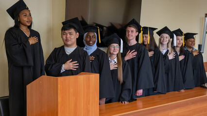 Graduates stand proudly at the ceremony with their hands over their hearts. 