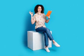 Young woman reading book while smiling in casual style on blue background