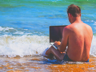 Working always and everywhere. Portrait of male entrepreneur working with laptop in the sea or ocean.  Copy space for design.