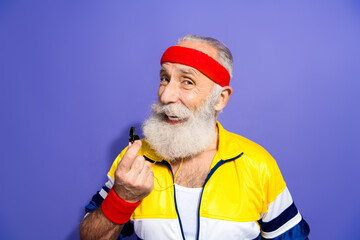 Funky man in retro sportswear with headband and whistle posing cheerfully on violet background