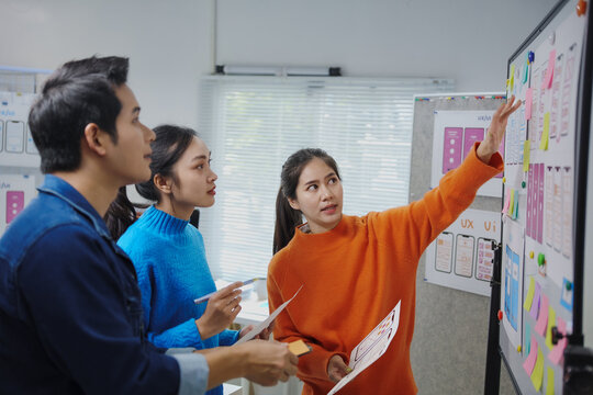 Web designers working together in the office using sticky notes and wireframes on a whiteboard, designing a new mobile app interface - Powered by Adobe