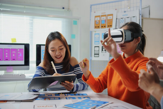 Asian women engaging in testing a virtual reality app and taking notes during a collaborative meeting in an innovative office setting