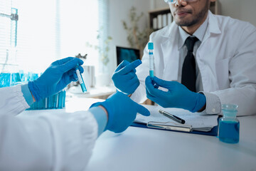 Medical researchers wearing lab coats and gloves are examining a test tube containing blue liquid...