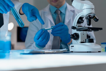 Medical researchers wearing lab coats and gloves analyzing a test tube containing blue liquid next to a microscope