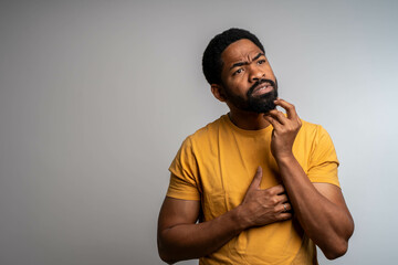 Thoughtful male customer thinking hard, looking away at copy space, leaning chin on hand. Handsome young man in casual t-shirt standing isolated over grey background. Special offer concept