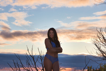Young, beautiful Latin woman in blue underwear standing in a forest in the golden hour at sunset....