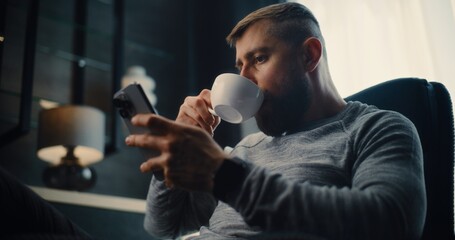 Professional Stock Exchange Trader Monitoring Real-Time Stocks and Exchange Market Charts Using Smartphone, Drinking Coffee. Successful Investment Agent Working in Cozy Office of Financial Agency.