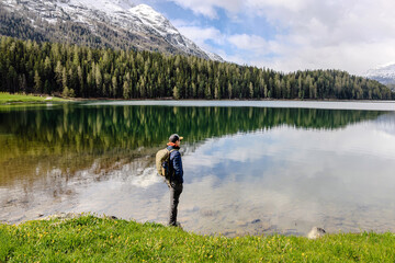 Fototapeta premium A hiker stands by a serene lake, reflecting the surrounding mountains