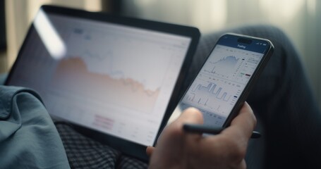 Close Up of Successful Businessman Working on Smartphone and Tablet Computer Displaying Real-Time Stocks and Exchange Market Charts in Online Trading App. Professional Financial Expert in Office.