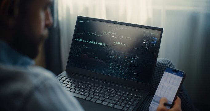 Close Up of Stock Exchange Trader Monitoring Real-Time Stocks and Exchange Market Charts in Online Trading App Using Smartphone and Laptop. Investment Agent Working in Office of Financial Agency.