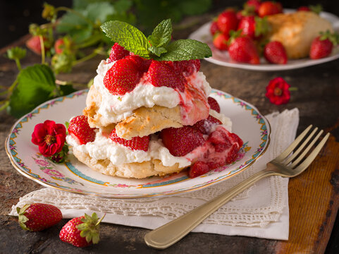 Homemade strawberry shortcake with whipped cream and mint garnish and a strawberry plant in the background