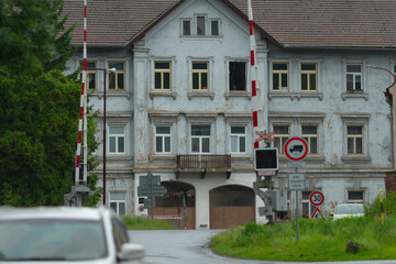 An abandoned building with a crumbling facade and road barriers shows neglect. Surrounded by wild grass, it creates an eerie atmosphere, ideal for exploration and photography