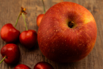 A vibrant red and yellow apple, ripe red cherries on a rustic wooden surface. the natural beauty and freshness of these popular fruits, perfect for themes of healthy eating and wholesome snacks