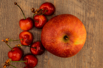 A vibrant red and yellow apple, ripe red cherries on a rustic wooden surface. the natural beauty and freshness of these popular fruits, perfect for themes of healthy eating and wholesome snacks