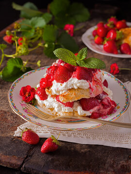 Homemade strawberry shortcake with whipped cream, mint as garnish, in a floral plate with parts of a strawberry plant in the background