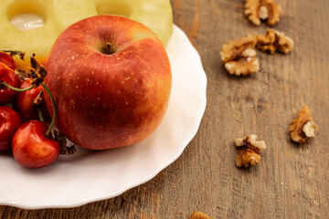 A red apple, pineapple rings, and red cherries are neatly arranged, with scattered walnuts adding a wholesome touch. This image perfectly captures a healthy and delicious snack. 
