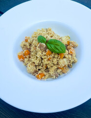 Colorful couscous with vegetables served in white plate, garnished with fresh basil.