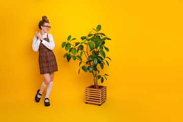 Cheerful teenage student posing with green plant against vivid yellow background, showcasing trendy...