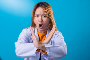 Serious Asian female doctor wearing white coat and orange shirt making crossed arms gesture in...
