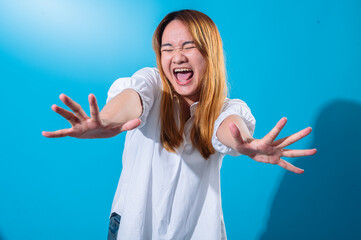 Asian woman with long straight hair in white shirt smiles widely and extends both hands forward in energetic open-palm gesture, standing against solid blue background in expressive studio portrait
