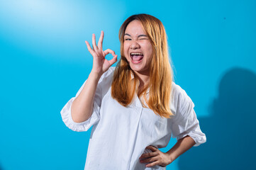 Asian woman with long straight hair in a white shirt smiles brightly while making an OK hand...