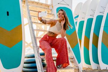 beautifil blond woman posing on summer beach in sunny weather using smartphone