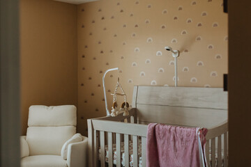 Modern Neutral Nursery with Wooden Crib, Boho Mobile, Accent Wallpaper, Cozy Glider Chair, and Soft Pink Blanket, Stylish Baby Room Interior Design Concept