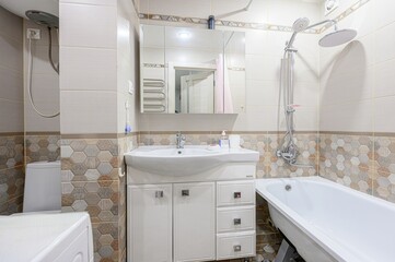 Bright bathroom featuring a white vanity, toilet, and bathtub, with tile walls in neutral tones and a decorative hexagonal pattern