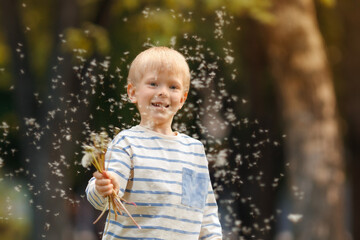 Close-up of cheerful child waving hand as dandelion seeds float around in soft spring light.