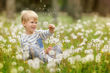 Excited boy waving his hand, surrounded by flying white dandelion seeds in soft spring air.