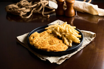 Pork or chicken Milanese, with french frieson plate on wooden table. Mediterranean, latin american food.