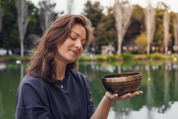 A young Caucasian woman yogi with long brown hair holds singing bowl for sound healing or...