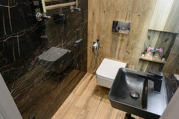 Stylish bathroom featuring black marble walls, light wood accents, modern fixtures including a...