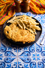 Pork or chicken Milanese, with french frieson plate on wooden table. Mediterranean, latin american food.