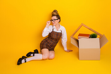 Young female student seated on a yellow background, wearing stylish plaid formalwear, with a box...