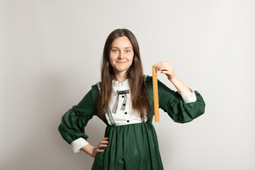 A woman with long hair smiles while holding a ruler in her right hand. She is wearing a green dress...