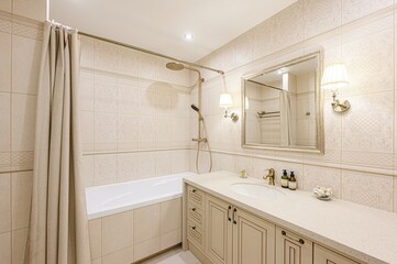 well-lit bathroom featuring beige tiles, a bathtub with a shower curtain, vanity with sink, and a framed mirror with sconces