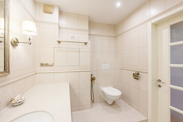 well-lit, beige-toned bathroom with tiled walls, a toilet, sink, and a partly-frosted glass door. Classic, clean, and functional design