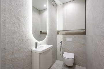 modern bathroom featuring textured gray tiles, a white vanity with a sink, an illuminated oval...
