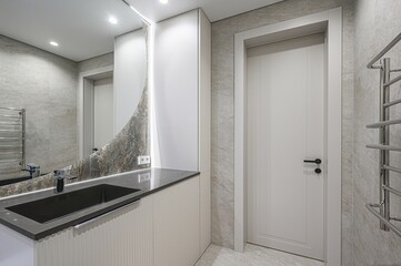 modern bathroom featuring a black sink, a curved mirror, a white door, and gray tile walls