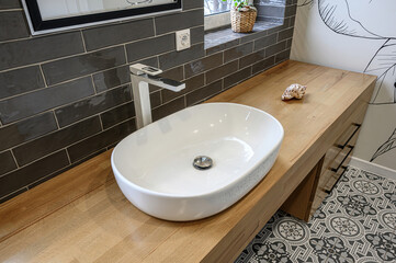 Fototapeta premium modern bathroom featuring a white oval sink, wooden countertop, and patterned tile floor. Dark grey brick-style tiles cover the wall