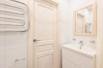 bright bathroom features white tiles, a light wood door, a sink vanity, a chrome towel warmer, and a matching framed mirror
