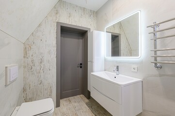 Modern bathroom with light tiles, a gray door, white vanity, and an illuminated mirror. Clean design with a minimalist aesthetic