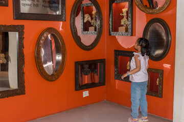 Adorable little girl child on her tiptoes exploring the mirror section of a museum. She gazes curiously at her own reflection, filled with wonder and excitement. childhood curiosity, learning