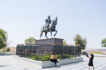 a young mother posing joyfully while her little daughter captures the moment on a mobile phone, on backdrop of the Maharana Pratap statue in Haldighati, Rajasthan. essence of travel, heritage, bonding