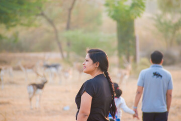 Beautiful Indian lady in black t-shrit with blurred background showing a man holding a child's hand and a herd of blackbucks in the grassland Tal Chhapar Wildlife Sanctuary. 