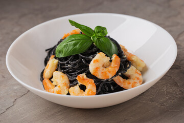 А plate of pasta with cuttlefish ink, shrimp, basil in cream sauce on stone background. Mediterranean cuisine.