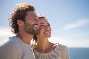 Happy couple smiling and looking up at the sky near the sea