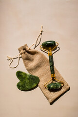 Skincare tools flat lay: gua sha scraper and jade roller on beige. Great for at home facial massage tutorials and natural beauty routines.