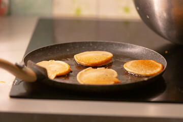 Pancakes are currently cooking on a frying pan situated on the stovetop in the kitchen, showcasing the delightful process of preparing a delicious breakfast food for your taste buds